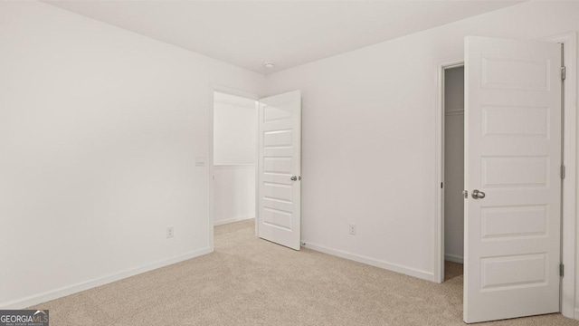unfurnished bedroom featuring baseboards, a spacious closet, a closet, and light colored carpet