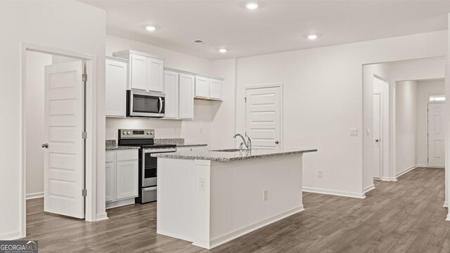 kitchen with stainless steel appliances, wood finished floors, a sink, a center island with sink, and white cabinetry