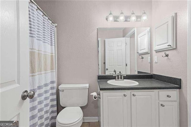bathroom featuring toilet, vanity, baseboards, and a textured wall