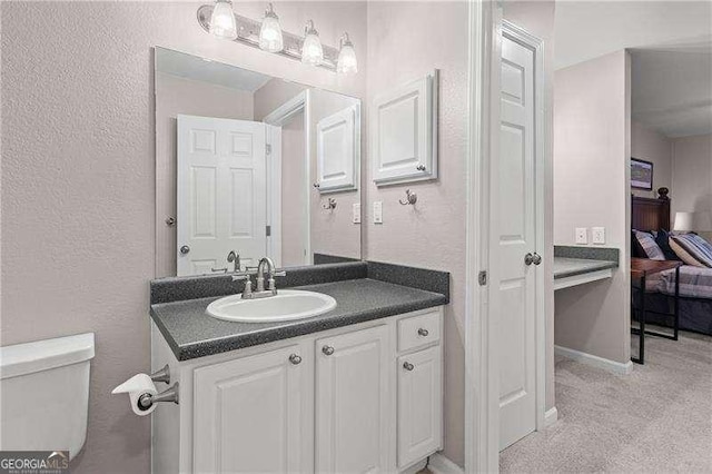 bathroom featuring vanity, toilet, a textured wall, and baseboards