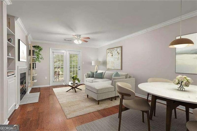 living area with baseboards, ceiling fan, a fireplace with flush hearth, ornamental molding, and wood finished floors