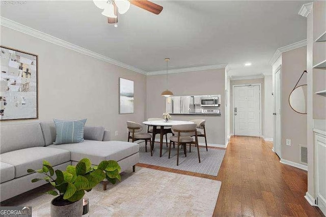 living area featuring a ceiling fan, visible vents, wood finished floors, baseboards, and ornamental molding