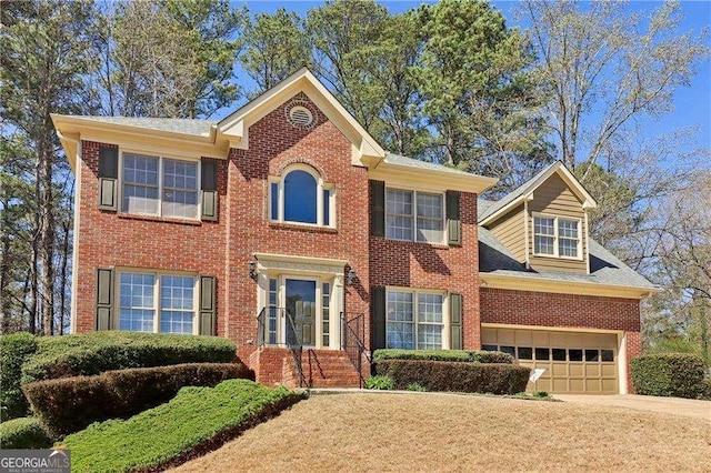 colonial house featuring brick siding, an attached garage, and driveway