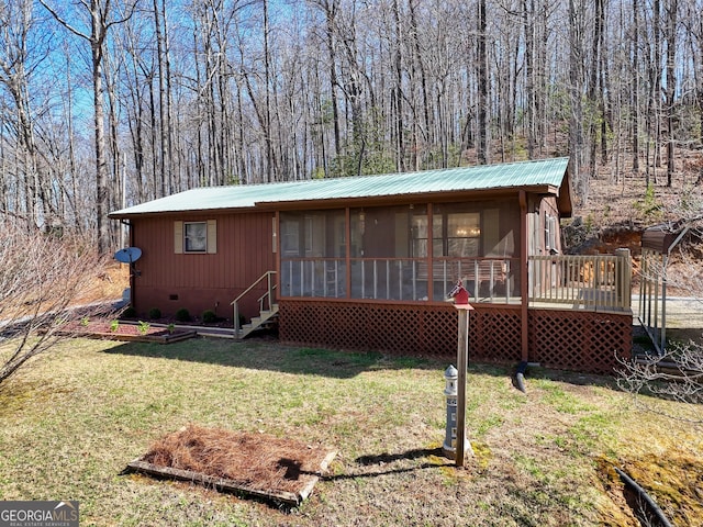 back of property with a wooded view, a sunroom, crawl space, a lawn, and metal roof
