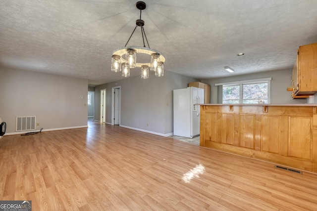 unfurnished living room featuring a textured ceiling, light wood-style floors, visible vents, and a chandelier