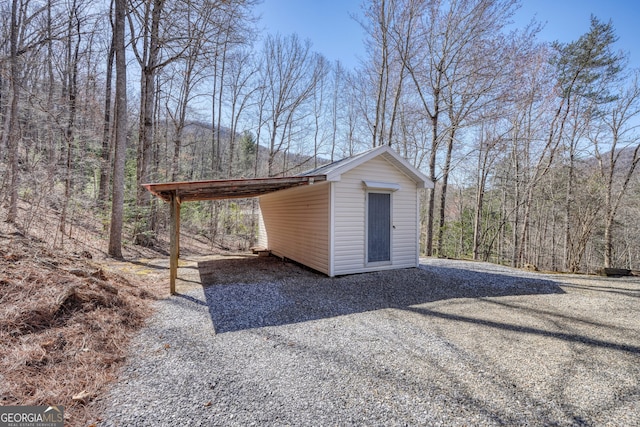 view of outbuilding with a view of trees, a carport, and an outdoor structure
