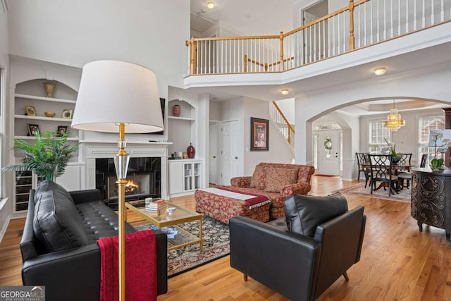 living room featuring stairs, arched walkways, a tiled fireplace, built in features, and wood finished floors