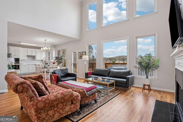 living area featuring a notable chandelier, a fireplace with flush hearth, light wood-style floors, and baseboards