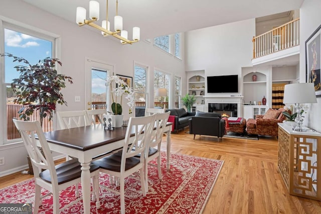 dining space featuring baseboards, light wood-style flooring, a glass covered fireplace, and a chandelier
