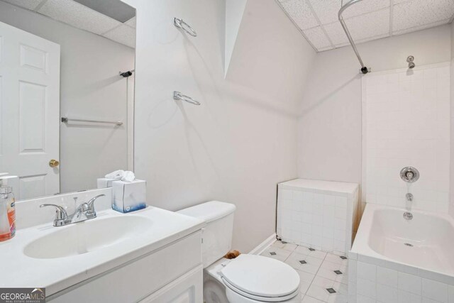 full bath featuring toilet, tiled shower / bath combo, a paneled ceiling, and vanity
