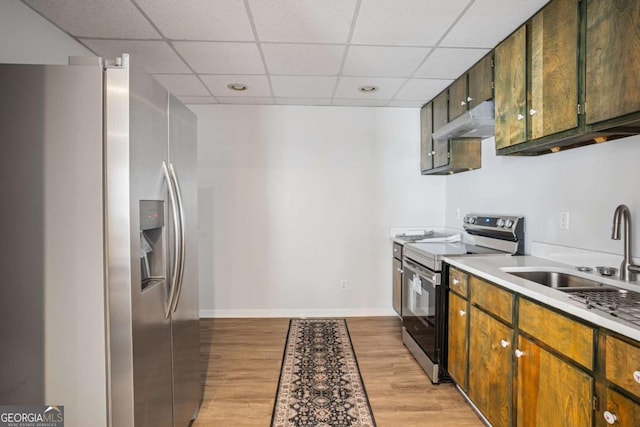 kitchen with a sink, light wood finished floors, appliances with stainless steel finishes, under cabinet range hood, and a paneled ceiling