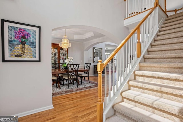 stairway with baseboards, ornamental molding, wood finished floors, a raised ceiling, and arched walkways