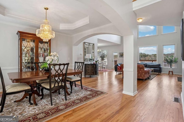 dining area with a tray ceiling, crown molding, a chandelier, light wood-style flooring, and arched walkways