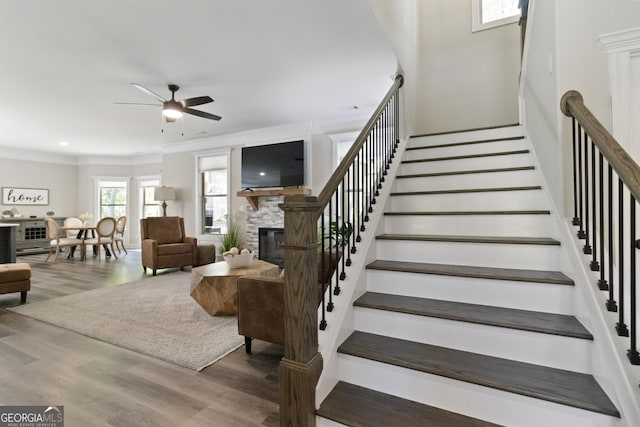 stairs featuring a ceiling fan, wood finished floors, a fireplace, and ornamental molding
