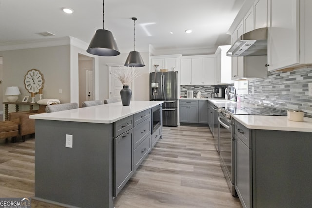 kitchen with stainless steel appliances, a sink, gray cabinetry, under cabinet range hood, and ornamental molding