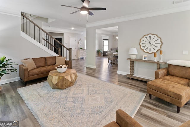 living area featuring stairway, crown molding, wood finished floors, ceiling fan, and baseboards