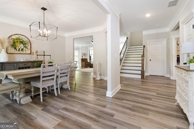 dining space with visible vents, ceiling fan with notable chandelier, wood finished floors, stairs, and crown molding
