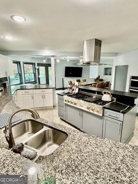 3810 Galloway Dr NE, Roswell, GA 30075 - kitchen with island range hood, stainless steel gas stovetop, a sink, white cabinets, and dark stone countertops