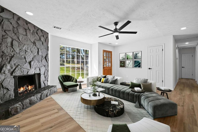 living area with a stone fireplace, a textured ceiling, ceiling fan, and wood finished floors