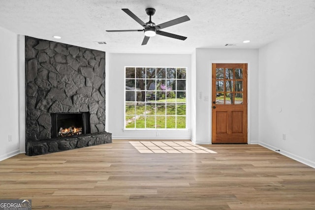 unfurnished living room with a fireplace, a textured ceiling, a ceiling fan, and wood finished floors