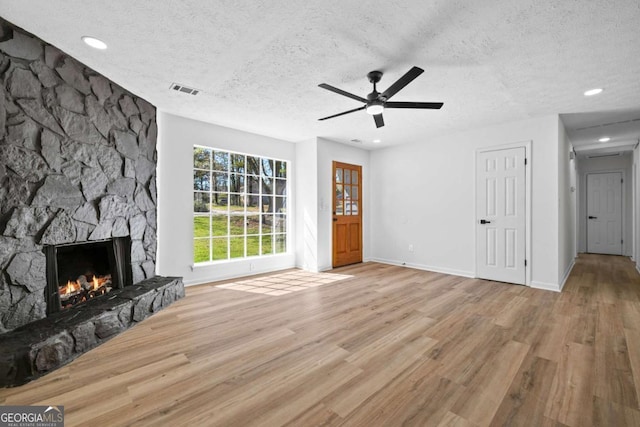 unfurnished living room with a stone fireplace, a textured ceiling, ceiling fan, and wood finished floors