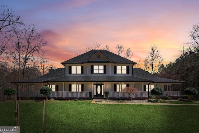 back of house at dusk featuring a porch, a chimney, a yard, and roof with shingles