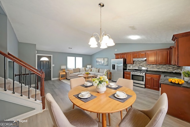 dining space featuring lofted ceiling, light wood-style flooring, a chandelier, and stairway