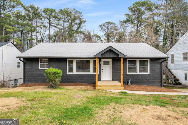 view of front of property featuring brick siding, a front lawn, and roof with shingles