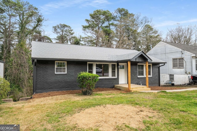 ranch-style home featuring brick siding, a front lawn, and roof with shingles