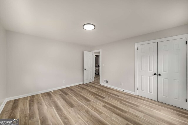 unfurnished bedroom featuring visible vents, baseboards, light wood-style floors, and a closet