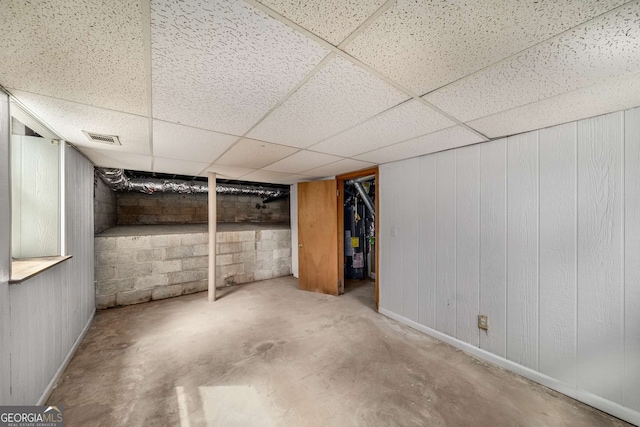 finished below grade area with water heater, visible vents, concrete block wall, and a paneled ceiling