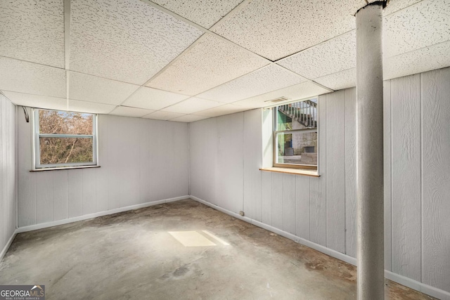basement with a paneled ceiling, baseboards, and wood walls