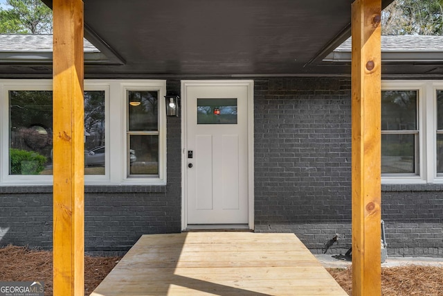 doorway to property with brick siding and roof with shingles