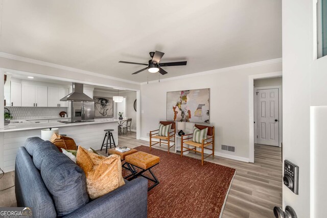 living area featuring a ceiling fan, baseboards, visible vents, light wood-style flooring, and ornamental molding