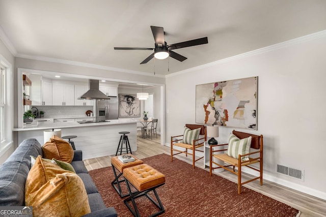 living area with visible vents, baseboards, ceiling fan, light wood-type flooring, and ornamental molding