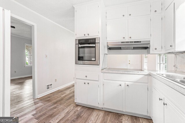 kitchen with under cabinet range hood, visible vents, white cabinetry, ornamental molding, and stainless steel oven