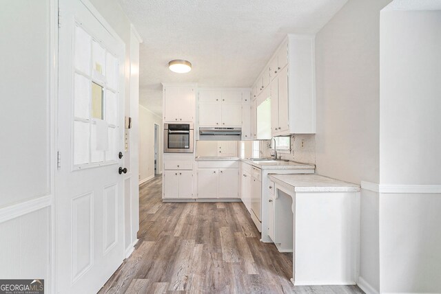 kitchen with light wood-style flooring, white cabinets, a sink, light countertops, and oven