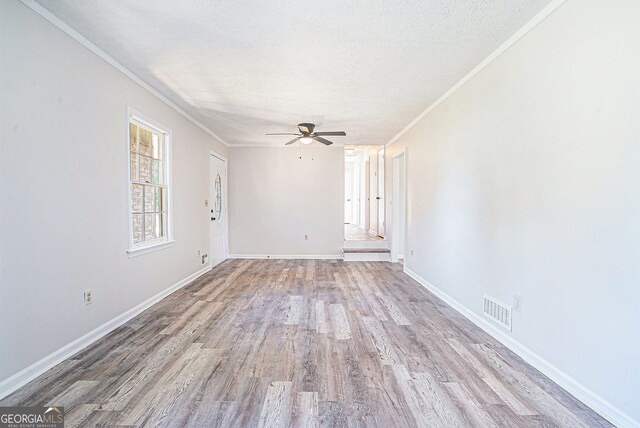 spare room featuring a textured ceiling, visible vents, ornamental molding, wood finished floors, and a ceiling fan