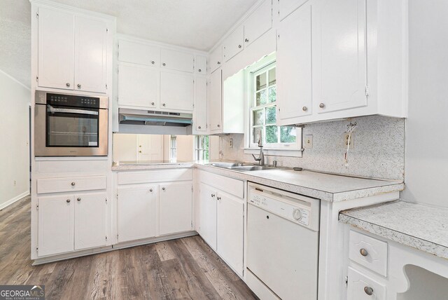 kitchen with a sink, under cabinet range hood, dishwasher, stainless steel oven, and wood finished floors