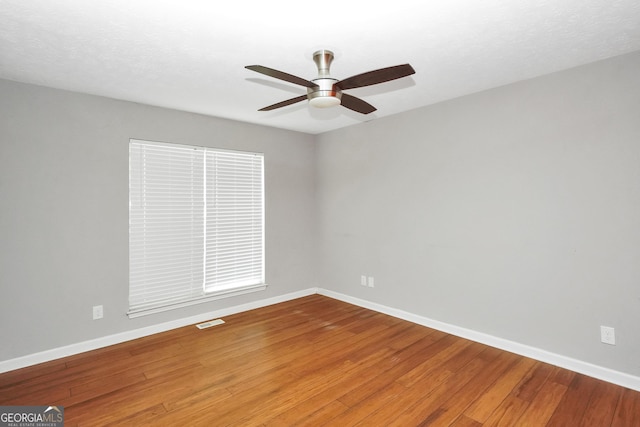 unfurnished room featuring wood finished floors, visible vents, a ceiling fan, and baseboards