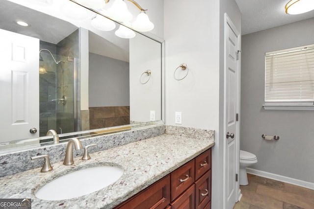 bathroom with baseboards, toilet, vanity, and tiled shower