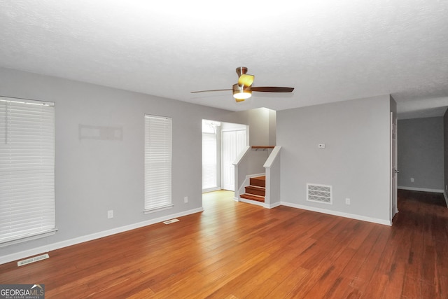 unfurnished living room featuring ceiling fan, wood finished floors, stairs, and visible vents