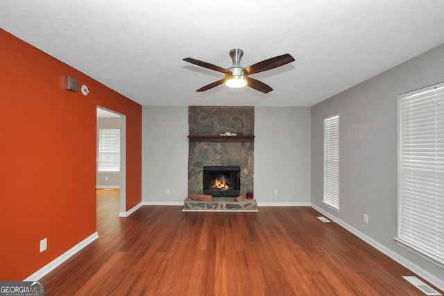 unfurnished living room featuring visible vents, baseboards, wood finished floors, ceiling fan, and a fireplace