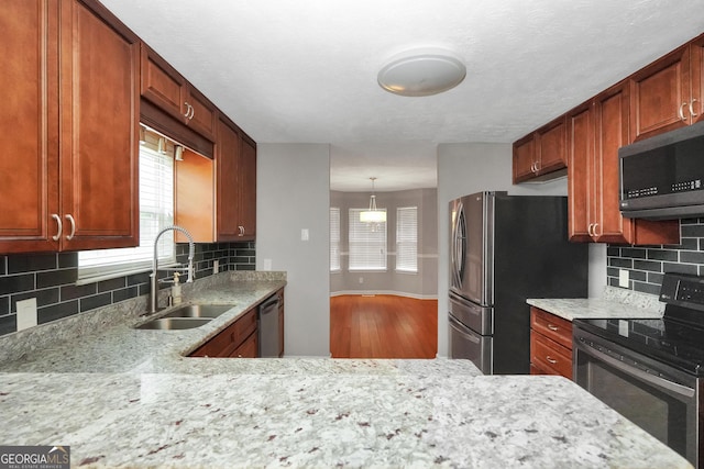 kitchen featuring stainless steel appliances, wood finished floors, a sink, baseboards, and decorative backsplash