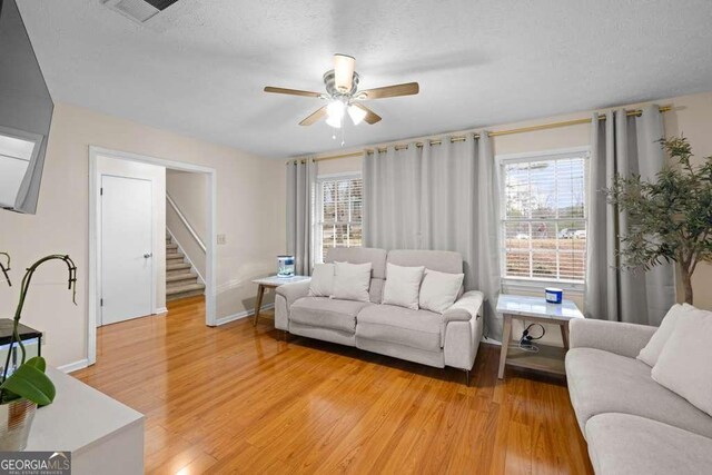 1417 Hickory Dr SW, Lilburn, GA 30047 - living area with stairway, light wood-type flooring, a ceiling fan, healthy amount of natural light, and a textured ceiling