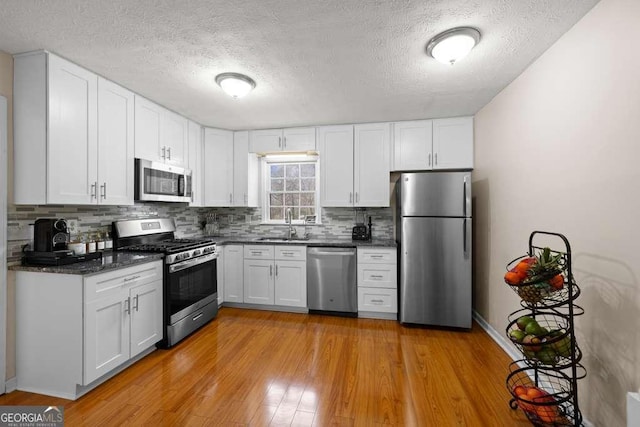 1417 Hickory Dr SW, Lilburn, GA 30047 - kitchen with stainless steel appliances, light wood-style floors, decorative backsplash, a textured ceiling, and white cabinetry