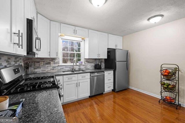 1417 Hickory Dr SW, Lilburn, GA 30047 - kitchen with stainless steel appliances, white cabinetry, backsplash, light wood-style floors, and a textured ceiling