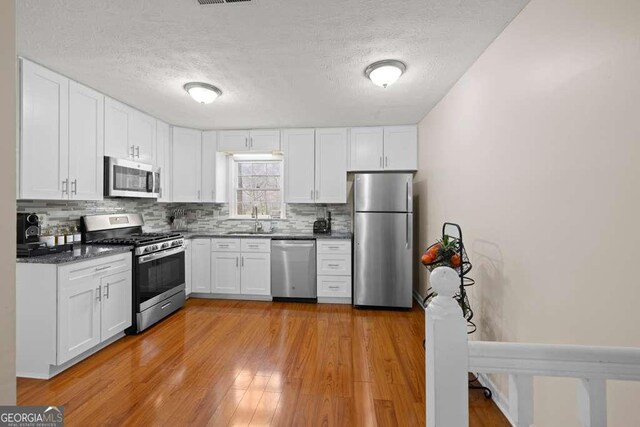 1417 Hickory Dr SW, Lilburn, GA 30047 - kitchen with appliances with stainless steel finishes, backsplash, white cabinets, a textured ceiling, and light wood finished floors