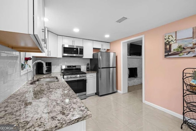 1417 Hickory Dr SW, Lilburn, GA 30047 - kitchen featuring stainless steel appliances, backsplash, light stone countertops, white cabinetry, and a premium fireplace