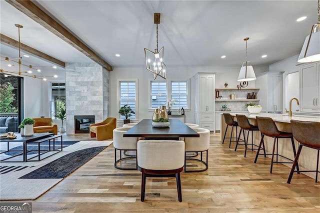 dining space featuring a fireplace, an inviting chandelier, light wood-type flooring, and beam ceiling